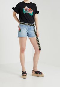 Camiseta negra con diseño floral y texto "Karl", combinada con pantalones cortos de mezclilla azul claro con bordados de flores y un cinturón negro y amarillo.