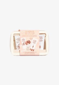 White zippered cosmetic pouch containing three skincare tubes. The label features light pink text with product details and rose gold accents.