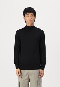 Maglione a collo alto nero realizzato in tessuto morbido, con maniche lunghe e polsini a costine. Presenta un motivo logo discreto sul petto.