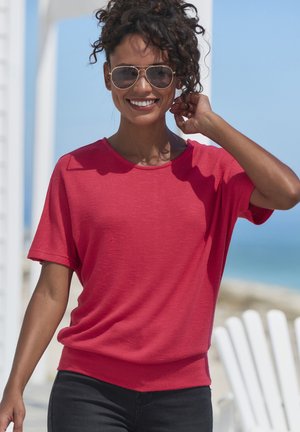 Red short-sleeve shirt with a relaxed fit, paired with black jeans. Fabric appears soft with a slight texture, suitable for casual wear.