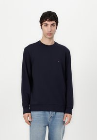 Navy blue sweatshirt made of cotton, featuring a round neckline and long sleeves, with a small logo accent on the chest. Worn with light blue jeans.