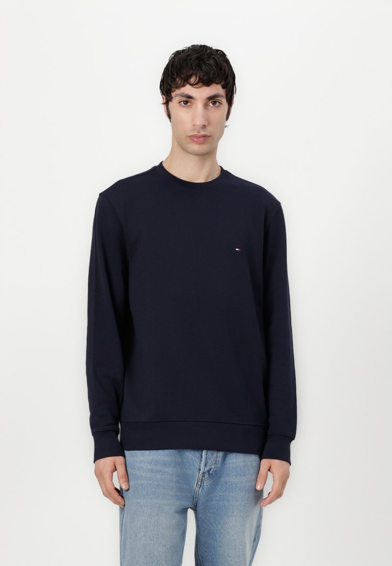 Navy blue sweatshirt made of cotton, featuring a round neckline and long sleeves, with a small logo accent on the chest. Worn with light blue jeans.