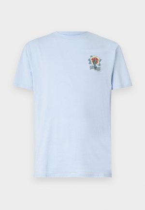 T-shirt en coton bleu clair, à manches courtes et col rond, avec un emblème graphique floral sur la partie gauche de la poitrine.