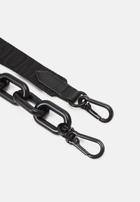 Sangle en tissu noire attachée à une chaîne en plastique noir épaisse avec deux mousquetons métalliques noirs sur fond blanc.