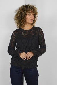 Schwarze Spitzenbluse mit filigranen floralen Mustern, langen Ärmeln und einem Rüschensaum. Getragen mit dunklen Jeans, die ein tailliertes Design betonen.