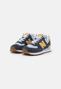 Paire de baskets bleu marine et gris avec lacets blancs, logo jaune "N" sur les côtés, et semelles couleur gomme présentées sur fond blanc.