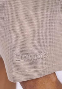 Bež shorts s teksturom izrađeni od materijala s uzorkom vafla, s diskretno izvezenim imenom branda na rubu.