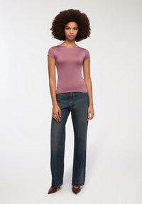 Top aderente a maniche corte in tessuto mauve, abbinato a jeans a gamba larga di colore blu scuro. La modella sta in piedi, indossando scarpe appuntite marroni.