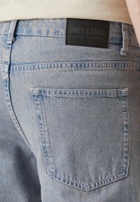 Jeans de mezclilla azul claros con un diseño de pierna recta, que cuentan con un bolsillo trasero y una etiqueta de cuero negro grabada con "ONLY & SONS."
