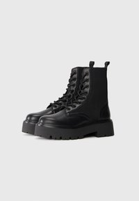 Black lace-up platform boots with thick rubber soles and fabric inset panels, shown side by side on a neutral background.