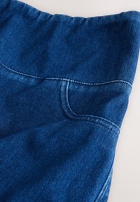 Primo piano di tessuto di denim blu con cuciture visibili e una cintura elastica.
