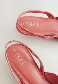 Sandale rose avec une finition en cuir brillant, design ouvert sur le devant, fines lanières, semelle intérieure rembourrée et nom de marque estampé "NEXT FOREVER COMFORT."