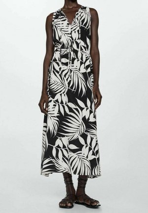 Schwarzes Maxikleid mit weißem tropischen Blattmuster; ärmelloses Design mit V-Ausschnitt und verstellbarem Taillenzug; kombiniert mit schwarzen Riemchensandalen.
