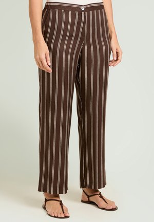 Pantalon marron à rayures verticales blanches porté avec des sandales noires à brides, montré de la taille aux pieds sur un fond uni.