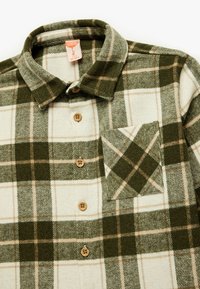 Grøn og flødefarvet plaid flannel skjorte med knapkrave, brune knapper og en lomme med et diamantmønster.