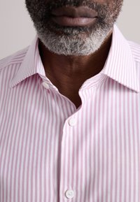 Roosa ja valge triibuline särk nööbitava kraega, tekstureeritud kangaga ja kaelas nähtavate nuppudega.