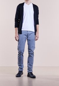 Námořnický cardigan, bílý tričko s V výstřihem, světle modré chinos kalhoty a černé tenisky. Cardigan má detail na knoflíky; chinos jsou úzkého střihu.