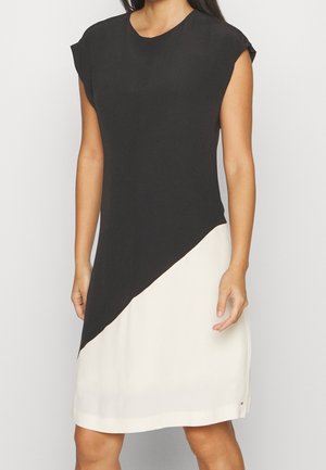 Kobieta w czarno-białej sukience bez rękawów z ukośnym, ukończonym pod kątem podziałem w talii.