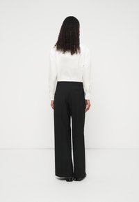 Mustad laiade jalgadega püksid, mis on sileda tekstuuriga, kõrge vöökohaga ja küljetaskutega, kombineeritud valge nööpidega särgiga, nähtuna tagantpoolt.