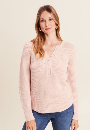 Maglione lavorato a maglia rosa chiaro con un motivo testurizzato, scollo a V con tre bottoni e maniche lunghe. Abbinato a jeans blu.