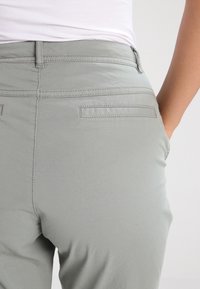 Jasnoszare spodnie o gładkiej fakturze, z tylnymi kieszeniami i tonowanym przeszyciem. Pas jest nieco podwyższony dla wygody.