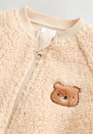 Beige fleece bomber jacket with a zip closure and a ribbed collar. Features a brown bear embroidery on the front. Soft texture.