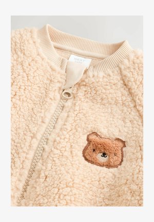 Beżowa bluza bombowiec z polaru, z zapięciem na zamek i ściągaczem u kołnierza. Na przodzie znajduje się haft z brązowym niedźwiedziem. Miękka tekstura.