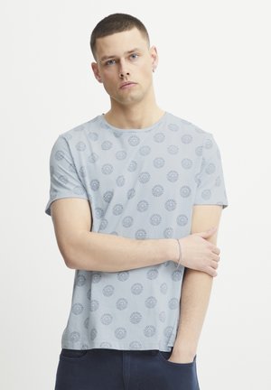 Hellblaues T-Shirt mit Rundhalsausschnitt und kurzen Ärmeln, das ein sich wiederholendes, kreisförmiges Muster in dunklerem Blau zeigt. Aus weichem Stoff gefertigt.