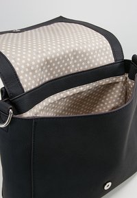 Svart läderhandväska med strukturerad yttermaterial och foder i prickigt tyg. Har en magnetisk stängning och ringdetalj på sidan.