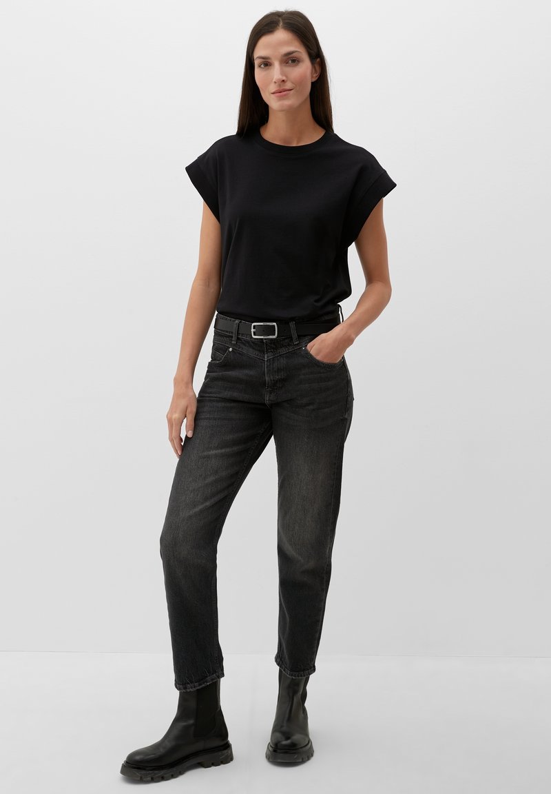 Zwarte shirt met korte mouwen, gecombineerd met donkergrijze jeans en zwarte enkellaarsjes. De outfit heeft een getailleerde silhouette en een minimalistisch ontwerp.
