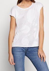 Bílý krátký rukáv top s perforovaným designem a kruhovými vzory. Vyrobeno z lehkého materiálu, má kulatý výstřih a volný střih.