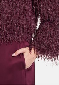 Pull en velours bourgogne avec de longues manches effilochées, associé à un tissu coordonné comportant une poche latérale et une finition lisse.