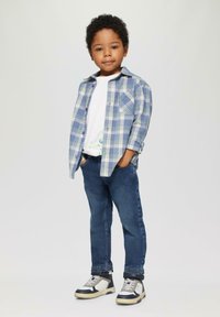 Blauwe en groene geruite overhemd over een wit T-shirt, gedragen met donkere spijkerbroek en multifunctionele sneakers.