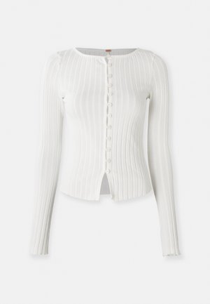 Witte geribbelde lange mouwen cardigan met ronde halslijn en tien voorknoopjes, licht aangepast met een kleine split aan de voorkant van de zoom.