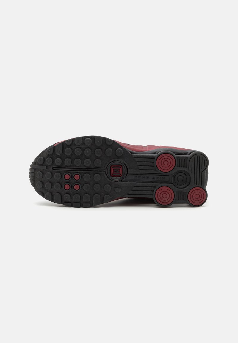 Semelle de chaussure de sport bordeaux avec caoutchouc noir, comportant des accents arrondis, des motifs circulaires et une texture antidérapante pour l'adhérence.