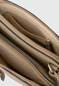 Interno della borsa in pelle beige caratterizzato da molteplici scomparti con cerniera e una fodera in tessuto liscia. Accenti neri lungo i bordi.