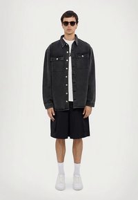 Mustast teksariidest särkjakk kahe rinnataskuga, nööpidega kinnitatav, kantud valge T-särgi peal, kombineeritud tumedate lühikeste pükste ja valgete tennistega.