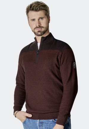 Bordeauxfarbener Reißverschluss-Pullover aus strukturiertem Strick, mit kontrastierenden schwarzen Schulterakzenten, gerippten Bündchen und Saum. Modell trägt ihn mit Denim.