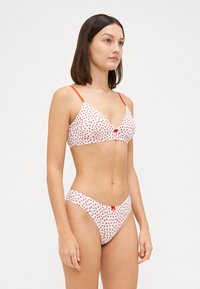 Triangle bikini set in white with red heart patterns. Features thin red straps and small decorative bow on the front of both pieces.