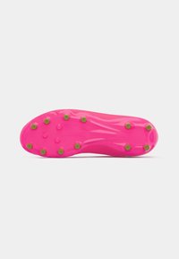 Bright pink soccer cleat sole with a smooth texture, featuring green studs and a contoured shape for traction and support on grass surfaces.