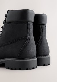 Čierne kožené topánky s textúrovaným povrchom, polstrovaným golierom, spevneným šitím a robustnou podrážkou s hlbokým profilom pre lepšiu priľnavosť.