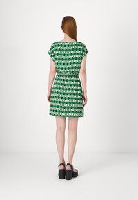 Abito verde a maniche corte con un motivo geometrico in bianco e nero, vita cintrata e taglio dritto che arriva sopra le ginocchia.