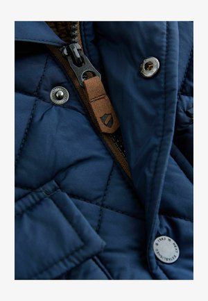 Tamnoplavi kviltani kaput s smešnim zatvaračem, metalnim dugmadi za snap i mekim unutarnjim oblogom. Sadrži dijagonalni uzorak šivanja.