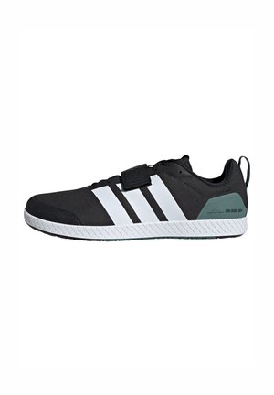 Black athletic shoe with a textured upper, three white stripes, a velcro strap, and a green accent on the heel. Features a rubber sole.