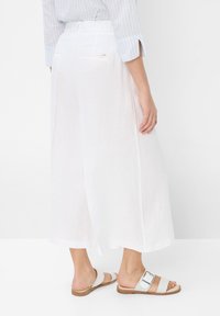 Culotte bianchi in lino con design a gamba larga e tasche posteriori, abbinate a sandali bianchi con una sola fascia e un dettaglio con fibbia.
