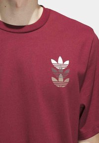 Camiseta de algodón burdeos con un logotipo de tres franjas en blanco serigrafiado en el lado izquierdo del pecho y un diseño clásico de escote redondo.