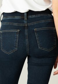 Donkerdenim jeans met een slim fit, voorzien van een hoge tailleband, twee achterzakken en gouden stikselaccenten op de naden.