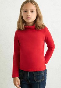 Maglione dolce a collo alto di colore rosso, realizzato in tessuto morbido, con maniche lunghe e design aderente, abbinato a jeans di denim scuro.