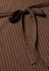 Tessuto marrone con sottili righe blu scuro. Presenta una cintura annodata al centro, evidenziando la texture e il motivo in un materiale morbido e liscio.