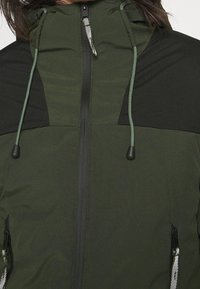 Mörkgrön ytterjacka med svarta detaljer, featuring dragkedjestängning, justerbar dragsko i huvan och fickor med dragkedja på sidorna.